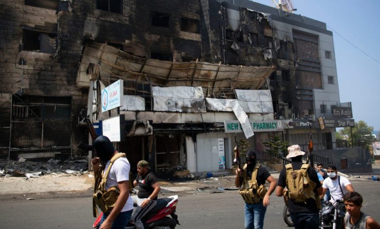 مسلّحون سنّة أمام مبنى أًضرمت فيه النيران في اشتباكات، خلال تشييع جنازة حسن زاهرغصن ، 14 عامًا. Photo Credit: AP