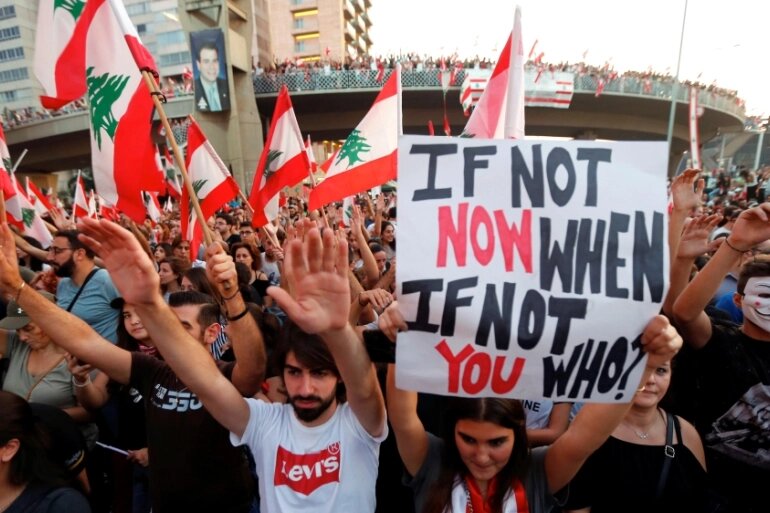 متظاهرون يرفعون الأعلام واللافتات خلال مظاهرة تشرين 2019. Photo Credit: Mohamed Azakir, Reuters